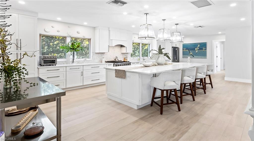Kitchen featuring white cabinets, a breakfast bar area, a large island with sink, hanging light fixtures, and light wood-type flooring