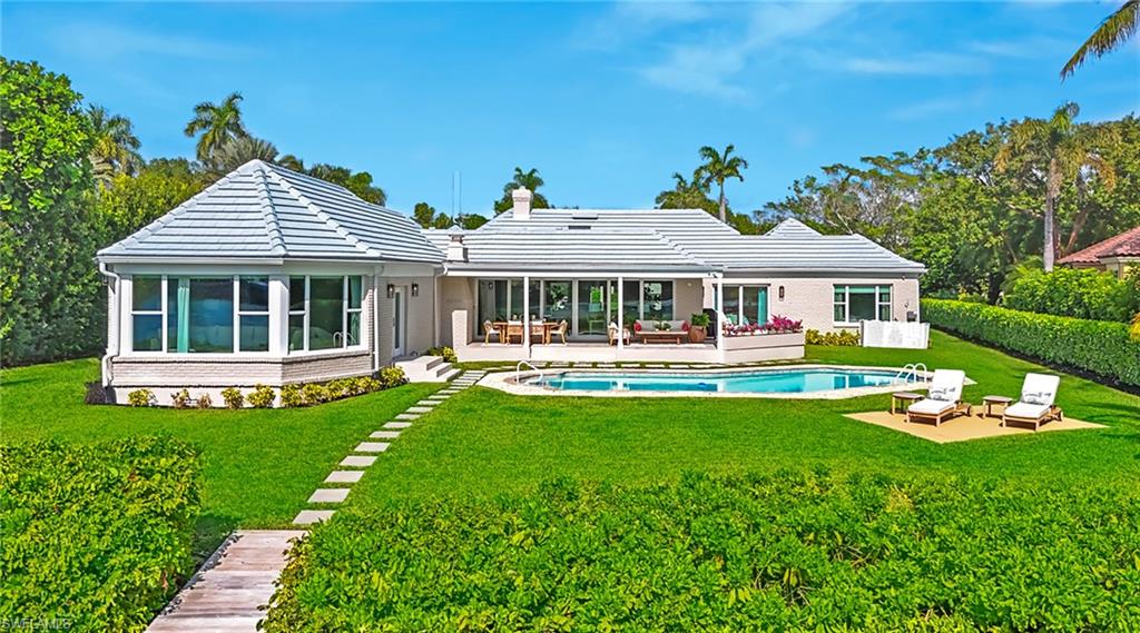 Back of property featuring a sunroom, a patio, a yard, an outdoor pool, and brick siding