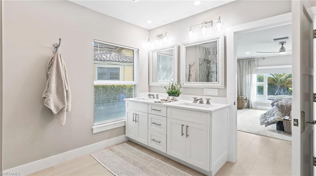 Ensuite bathroom featuring double vanity, ceiling fan, light wood-style floors, and a shower