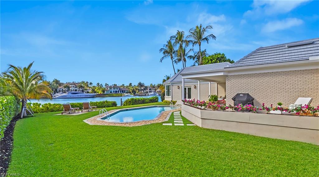 View of swimming pool with a lawn, patio surround, a water view, and grilling area