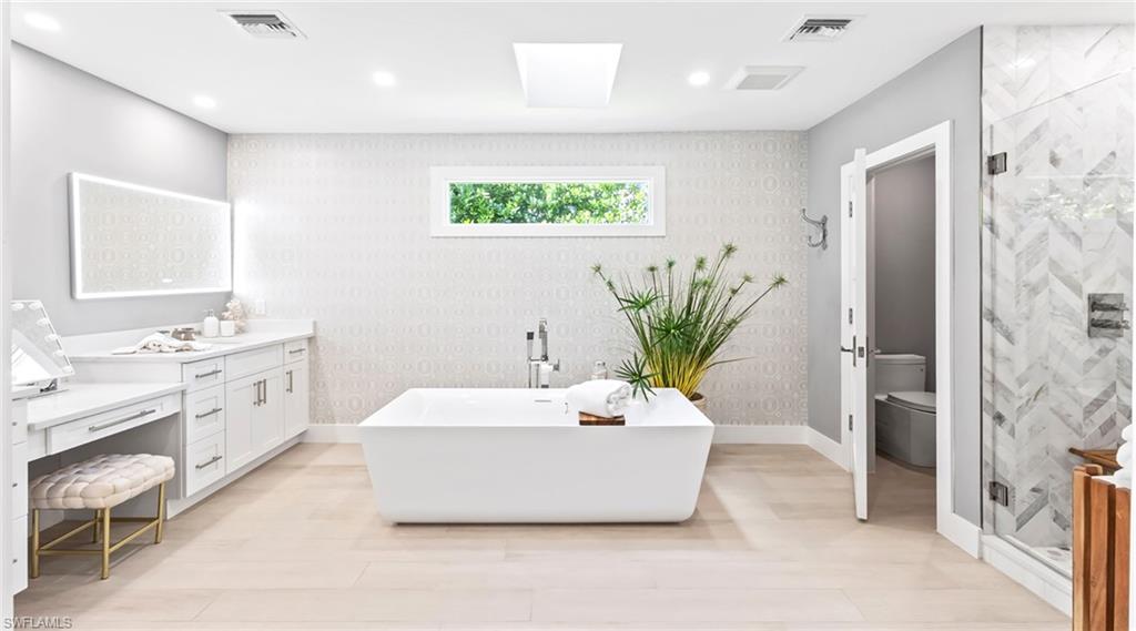 Bathroom featuring vanity, a freestanding bath, a stall shower, wallpapered walls, and light wood finished floors