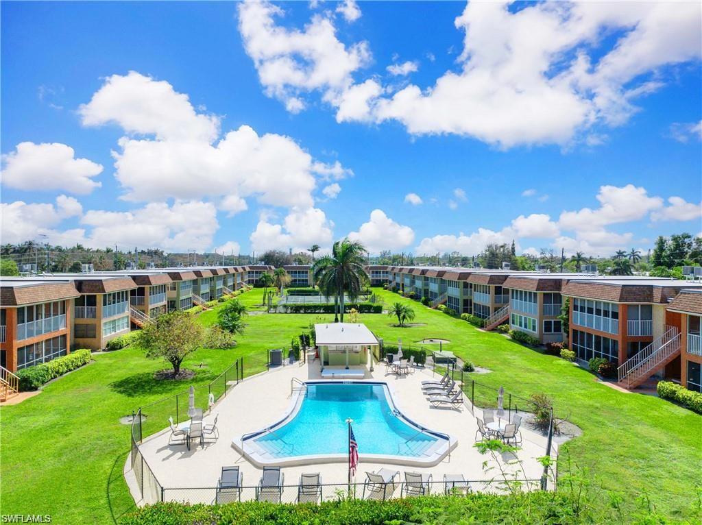 Community pool surrounded by open green space and low-rise condominium buildings.