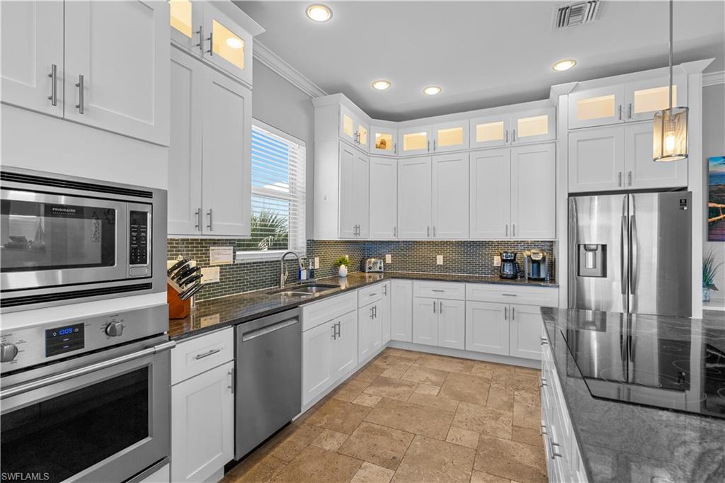 Modern kitchen featuring white cabinetry, stainless steel appliances, granite countertops, a mosaic tile backsplash, and light-toned tile flooring