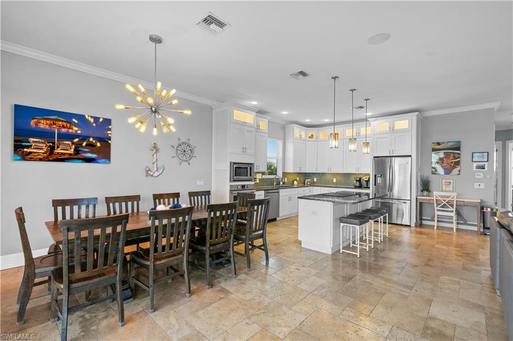 Open-concept kitchen and dining area featuring a prominent kitchen island with seating, stainless steel appliances, white cabinetry with upper glass-front elements, and a tiled backsplash