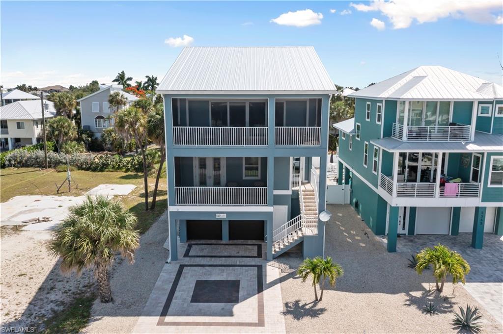 Three-story coastal residence featuring a metal roof, screened balconies, an exterior staircase, and ground-level parking