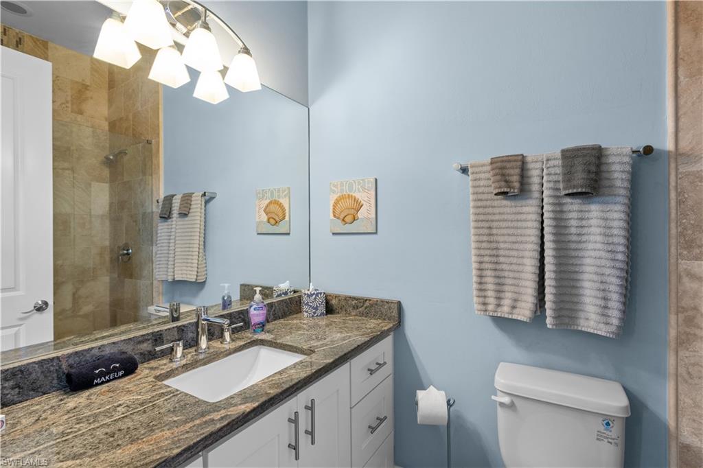 Bathroom featuring a granite countertop vanity with an undermount sink, white cabinetry, a glass-enclosed shower with tile surround, and a coordinating wall-mounted light fixture