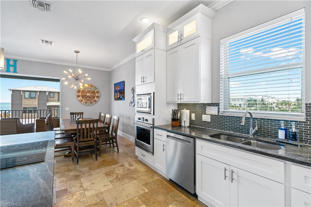 Modern kitchen featuring white cabinetry, stainless steel appliances, granite countertops, and a dark tile backsplash