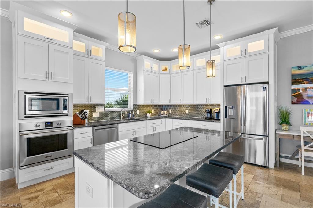 Spacious kitchen featuring white cabinetry, a large center island with a cooktop, stainless steel appliances, and a tiled backsplash