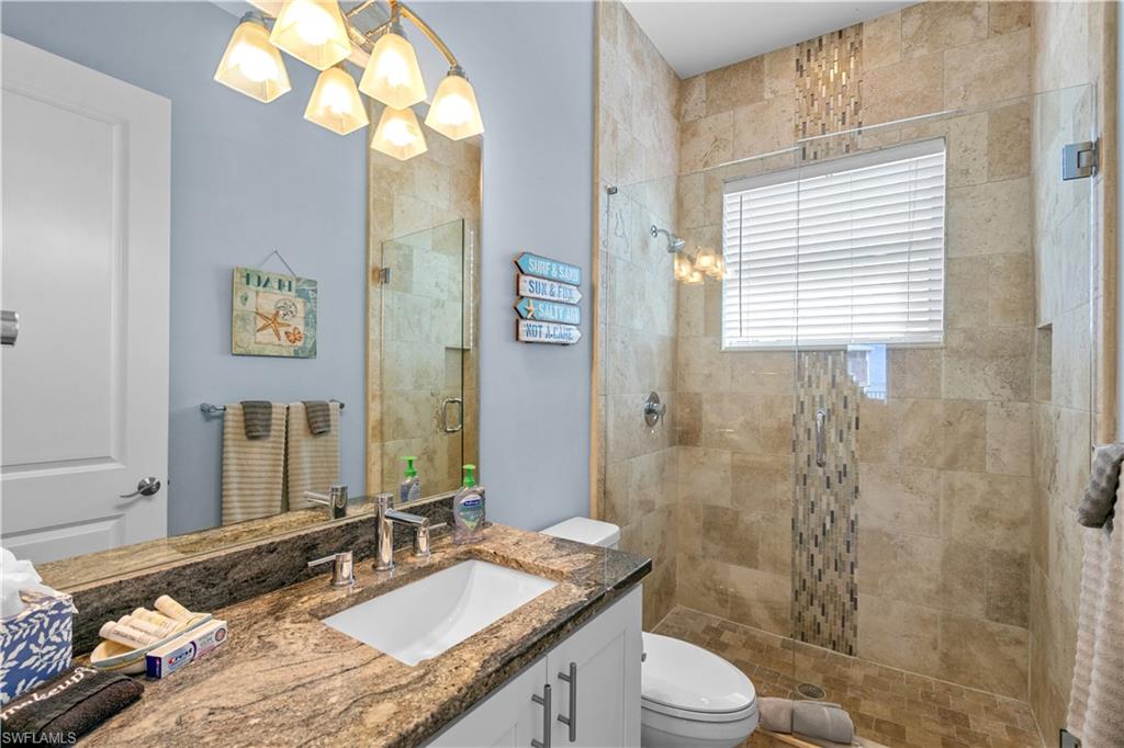 Bathroom featuring a granite countertop vanity with an undermount sink, a tiled walk-in shower with a glass enclosure, a mosaic tile accent strip, and a window with blinds