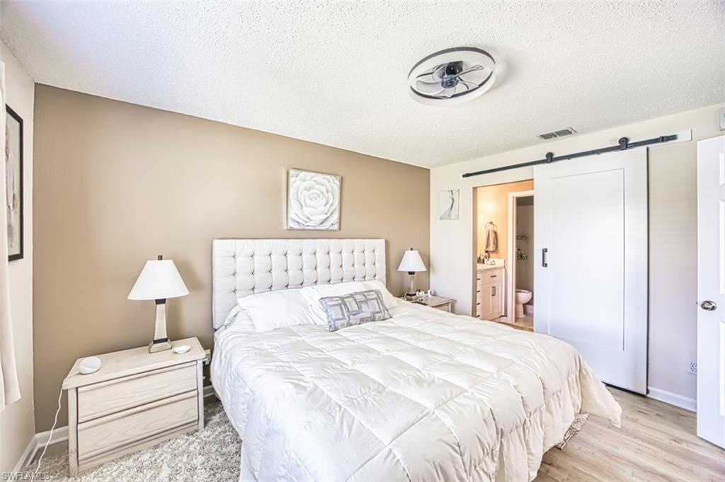 Bedroom with a barn door, a textured ceiling, light wood finished floors, ensuite bathroom, and baseboards