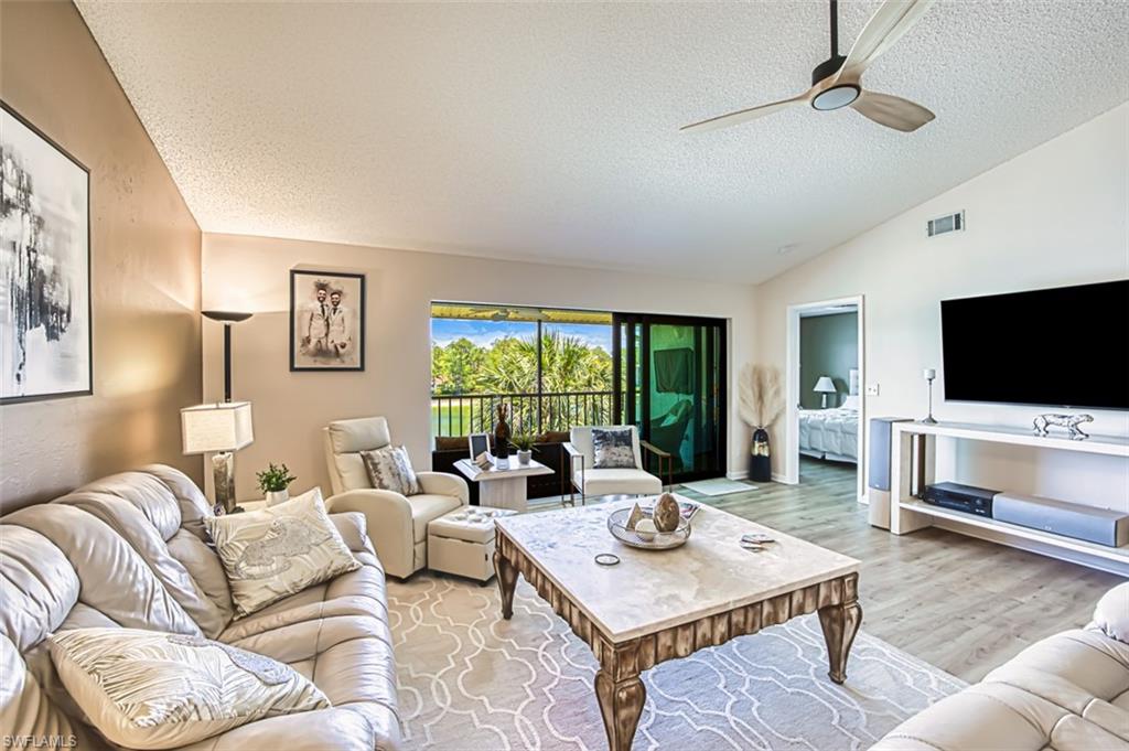 Living area featuring a textured ceiling, vaulted ceiling, ceiling fan, and light wood finished floors