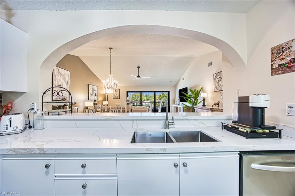Kitchen featuring a sink, dishwasher, vaulted ceiling, light stone countertops, and pendant lighting