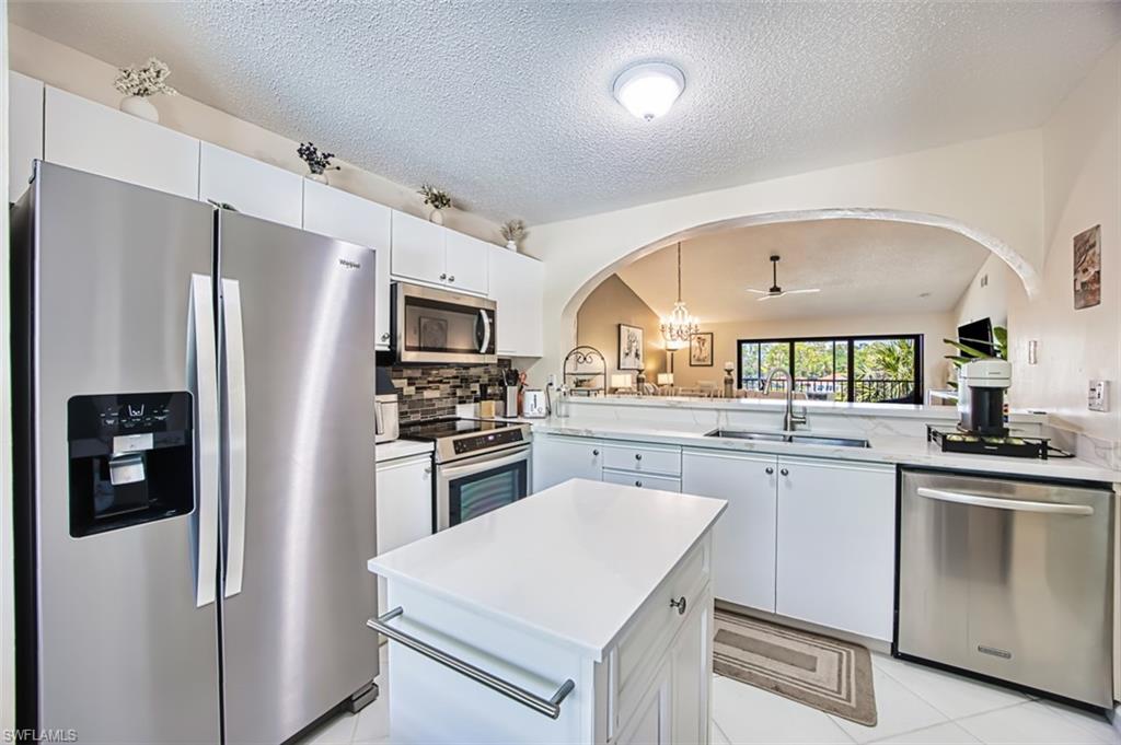 Kitchen with appliances with stainless steel finishes, a sink, arched walkways, light countertops, and a textured ceiling