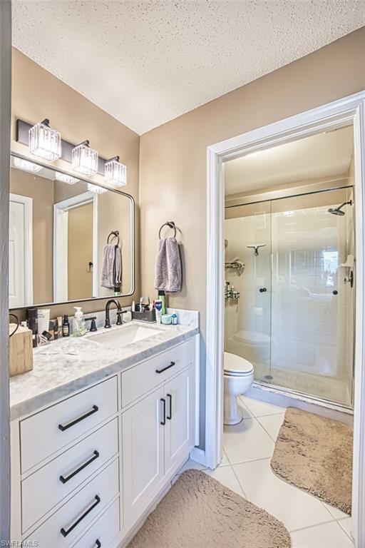 Bathroom featuring a stall shower, toilet, vanity, tile patterned flooring, and a textured ceiling