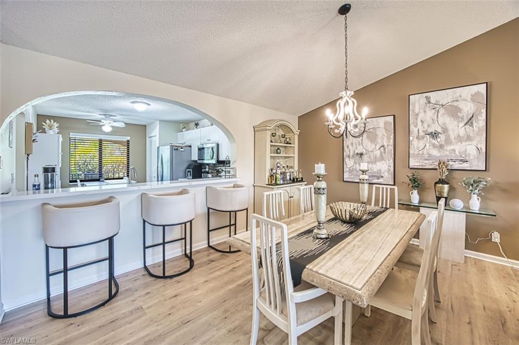 Dining area featuring arched walkways, light wood-style flooring, vaulted ceiling, a ceiling fan, and a textured ceiling
