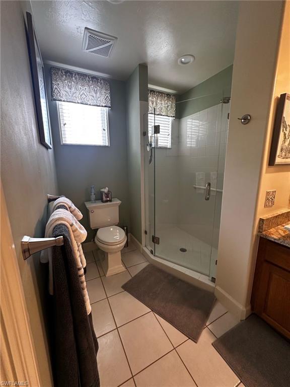 Full bathroom featuring tile patterned flooring, visible vents, toilet, a wealth of natural light, and a stall shower