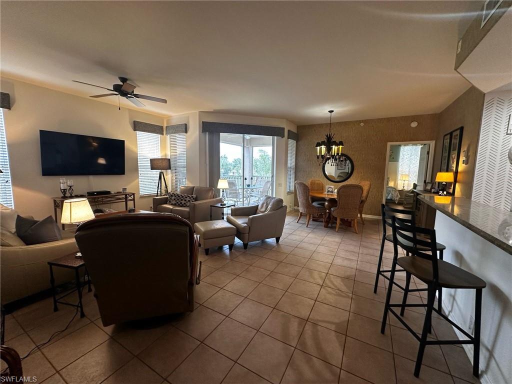 Tiled living room featuring ceiling fan with notable chandelier and wallpapered walls