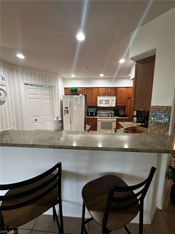 Kitchen with a peninsula, a kitchen breakfast bar, white appliances, and brown cabinets