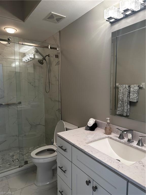 Full bath with vanity, toilet, a marble finish shower, marble finish floor, and visible vents