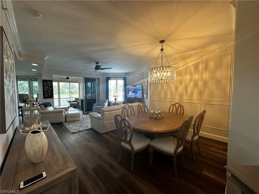 Dining space featuring ornamental molding, ceiling fan with notable chandelier, and dark wood-style flooring