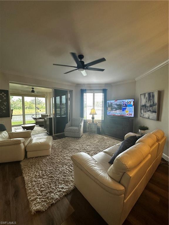Living room featuring ornamental molding, a ceiling fan, and dark wood-style floors