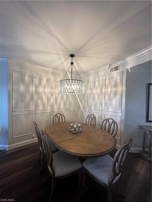 Dining area with visible vents, ornamental molding, dark wood-style floors, and a notable chandelier
