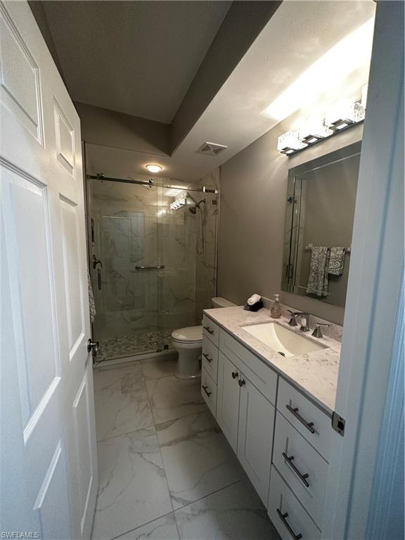 Full bathroom featuring visible vents, vanity, toilet, marble finish floor, and a marble finish shower