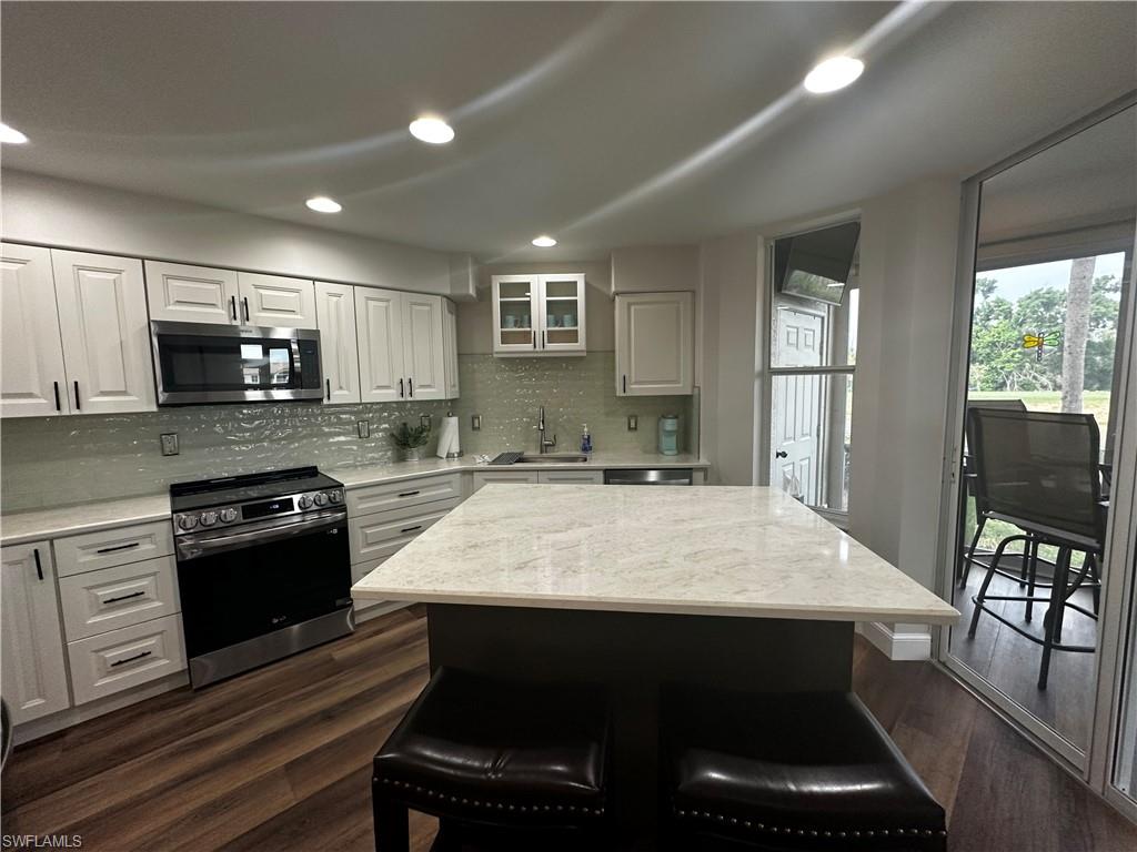 Kitchen with a sink, dark wood finished floors, appliances with stainless steel finishes, and a kitchen breakfast bar