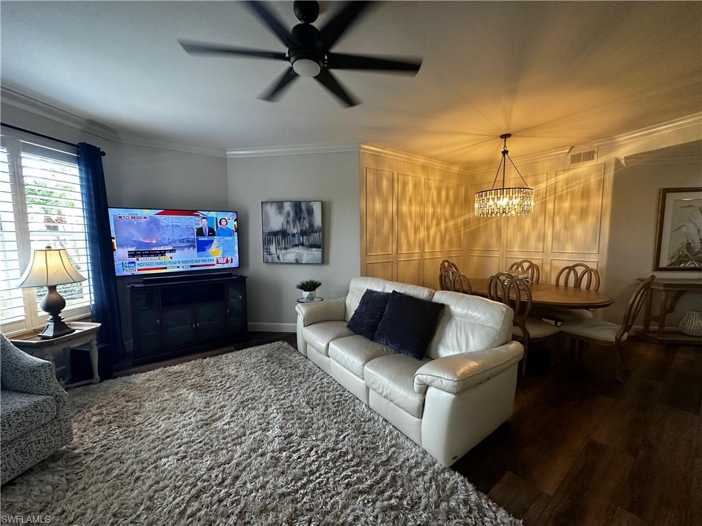 Living area with crown molding, ceiling fan with notable chandelier, baseboards, wood finished floors, and visible vents