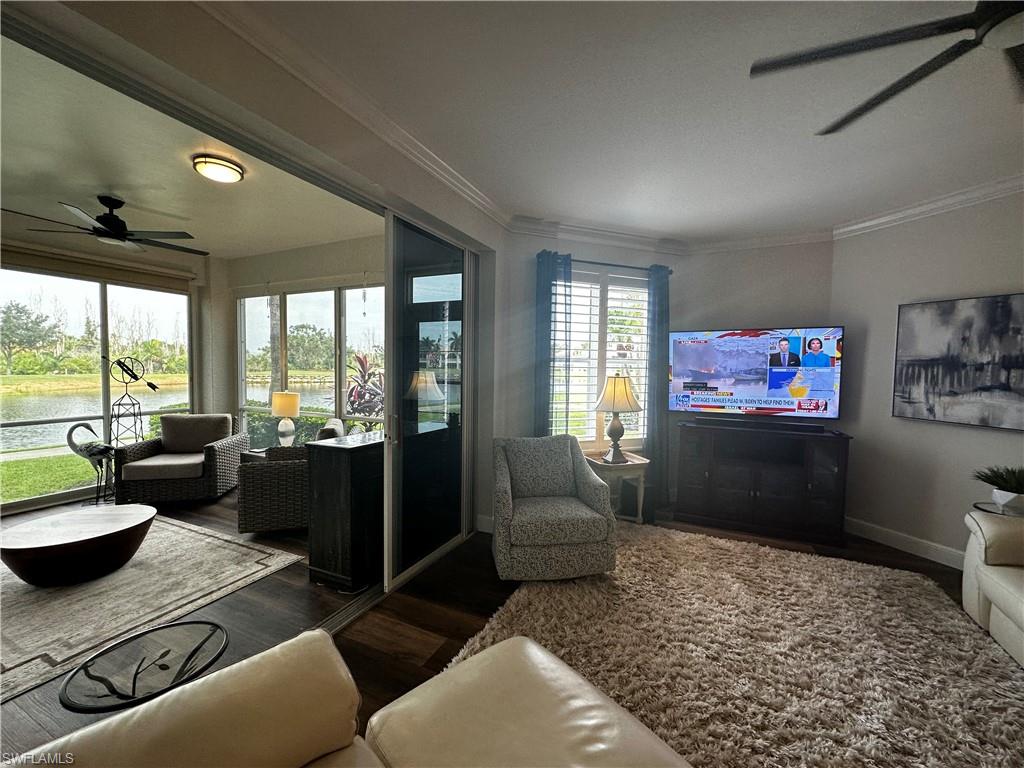 Living area with crown molding, wood finished floors, baseboards, a water view, and a ceiling fan
