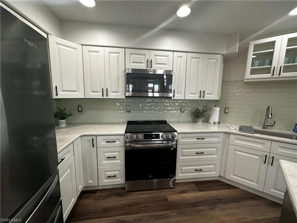 Kitchen with white cabinets, dark wood-style flooring, appliances with stainless steel finishes, backsplash, and glass insert cabinets