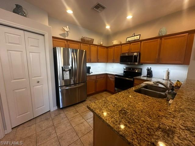 Kitchen with dark stone countertops, a sink, brown cabinetry, appliances with stainless steel finishes, and visible vents