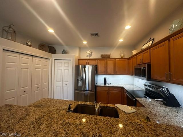Kitchen with a sink, dark stone counters, visible vents, brown cabinets, and appliances with stainless steel finishes