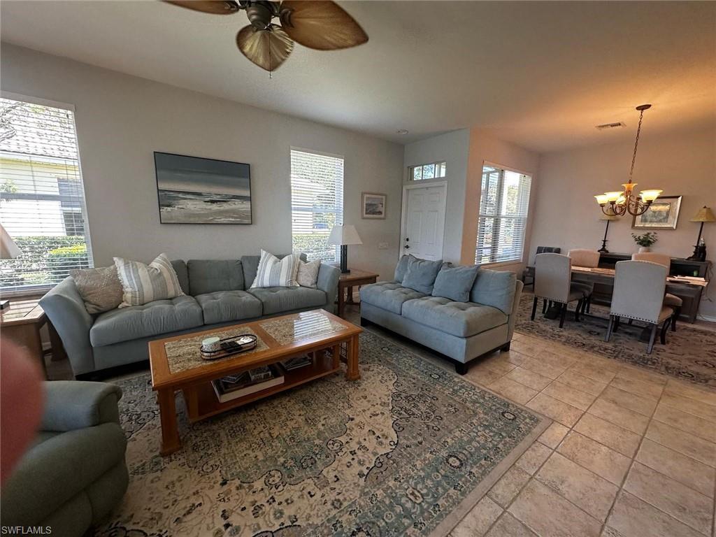 Living area with light tile patterned flooring, ceiling fan with notable chandelier, and plenty of natural light