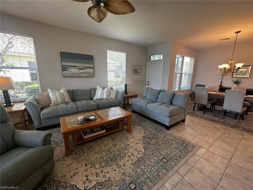 Tiled living room with visible vents and ceiling fan with notable chandelier