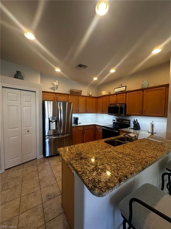 Kitchen featuring brown cabinets, a peninsula, stainless steel appliances, and a sink