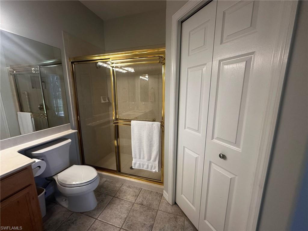 Bathroom featuring a closet, a stall shower, vanity, toilet, and tile patterned flooring