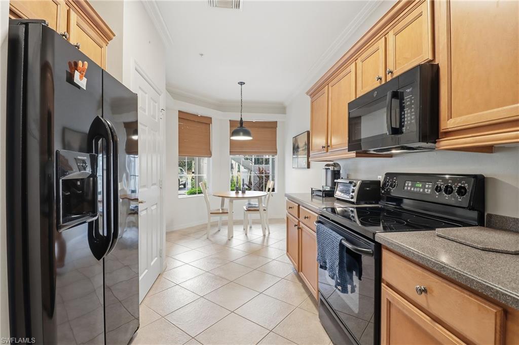 Kitchen with black appliances, crown molding, pendant lighting, light tile patterned flooring, and dark countertops