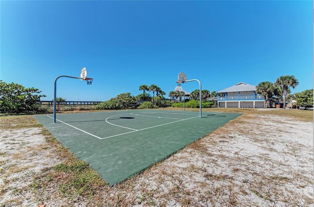 Outdoor basketball court with two hoops, surrounded by natural landscaping and sand