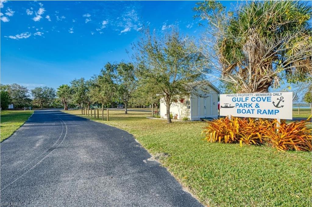 Paved private road leading to a designated members-only park and boat ramp, bordered by mature trees and manicured lawn