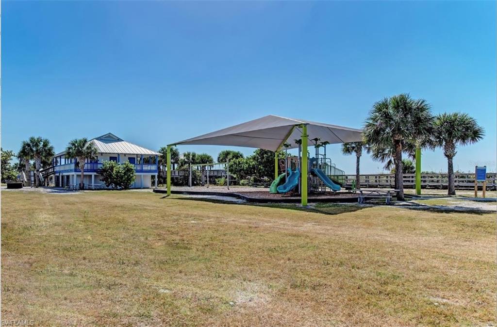 Expansive green space featuring a shaded playground structure, mature palm trees, and a distant two-story property with balconies