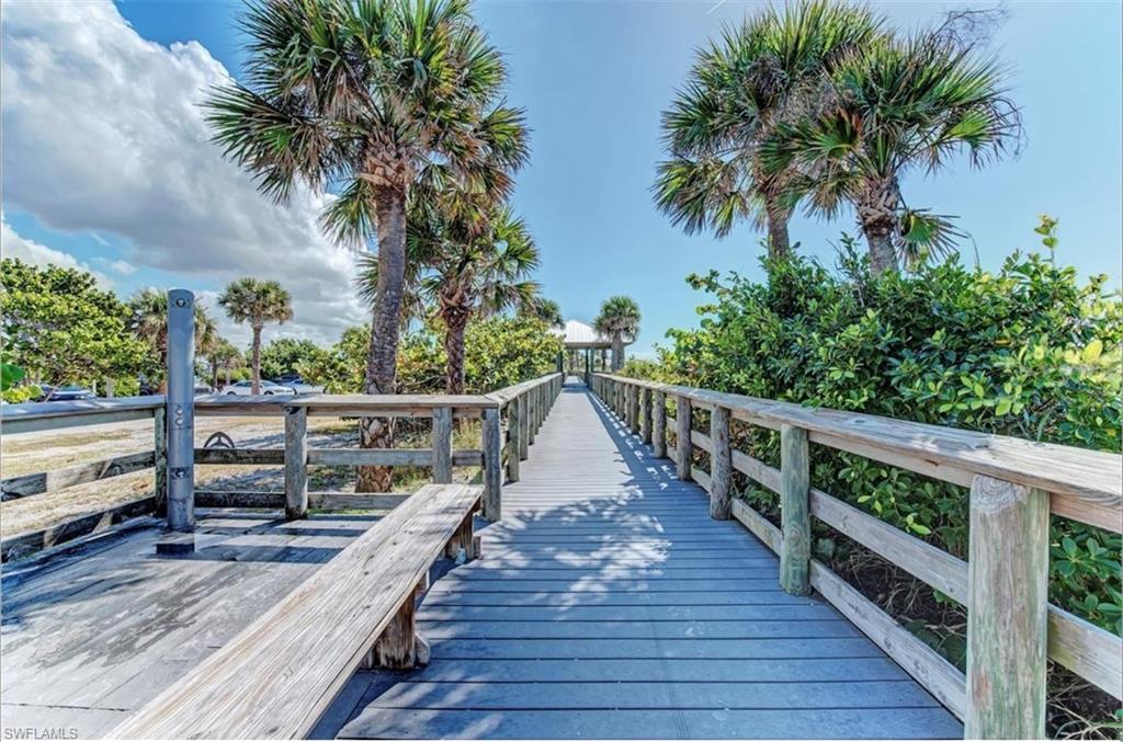 Expansive elevated wood-finish walkway with natural wood railings, surrounded by lush tropical landscaping and mature palm trees