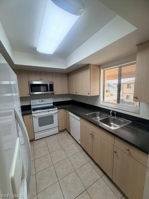 Bright kitchen featuring light wood-finish cabinetry, dark countertops, a double stainless steel sink, and a white electric range with a stainless steel microwave