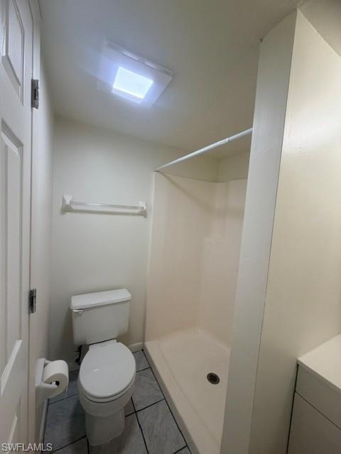Compact full bathroom featuring a white toilet, integrated shower stall, and light-toned tile flooring