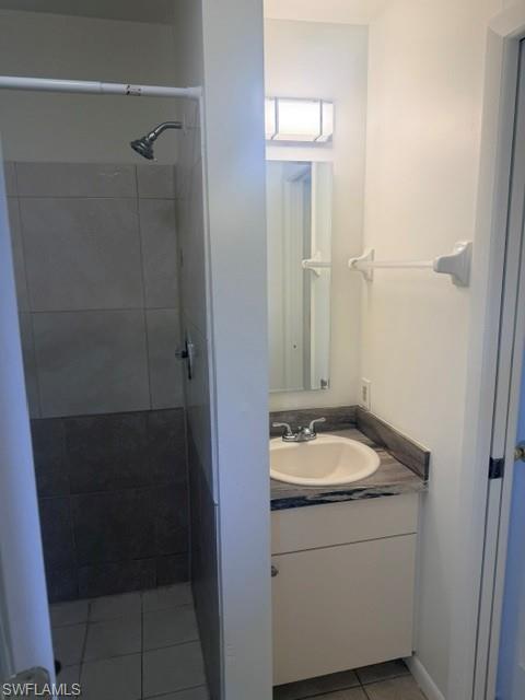 Bathroom featuring a white vanity with an undermount sink, granite-finish countertop, and a tiled shower enclosure