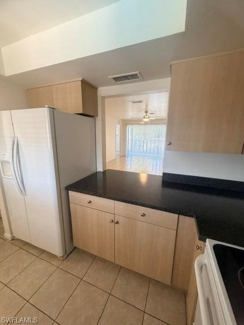 Kitchen featuring blonde wood-finish cabinetry, dark speckled countertops, and ceramic tile flooring