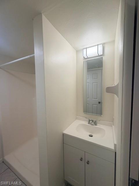 Compact bathroom featuring a white vanity with integrated sink, rectangular mirror, and an overhead vanity light