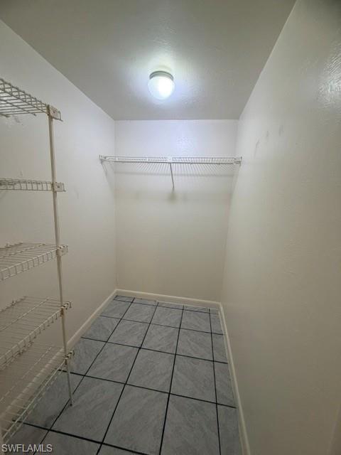 Utility space featuring a surface-mounted ceiling light, white wire shelving, a single wire hanging rod, and gray square floor tiles