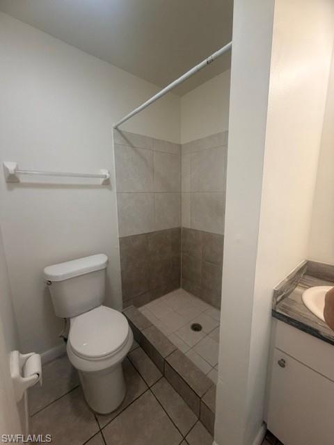Bathroom featuring a tiled shower stall with a low threshold, a white toilet, and a vanity with a gray stone-finish countertop