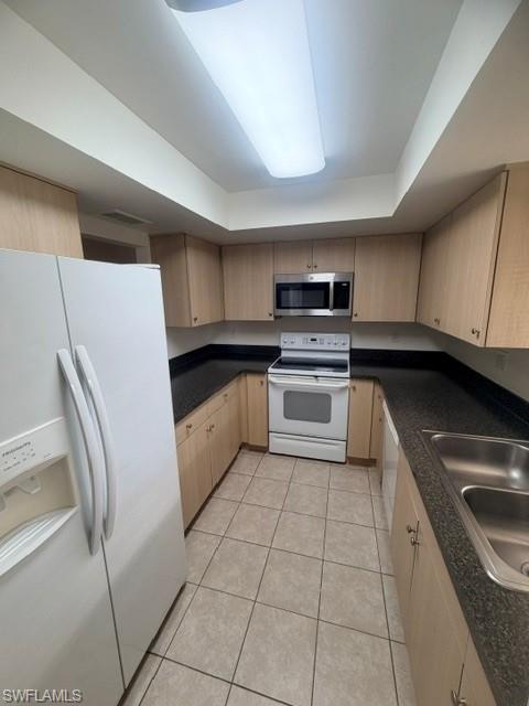 U-shaped kitchen featuring light wood-finish cabinetry, dark speckled countertops, and tile flooring